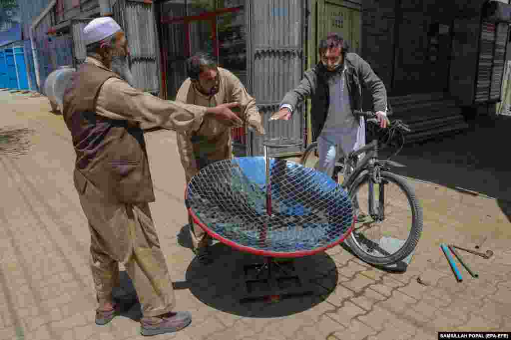 Onlookers feel the heat of the sun as Abbas (center) tests his newest stove. Proponents of solar stoves say that dishes can be prepared in the same amount of time as using a fireplace or gas stove, with the added benefit that they do not create pollution that leads to global warming.&nbsp;