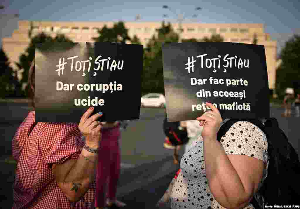 Two women shield&nbsp;their faces from the sun with signs reading in Romanian &quot;They all knew -- but corruption kills&quot; and &quot;They all knew -- but they&#39;re all the same mafia&quot; during a protest against the ruling parties&#39; coalition in the front of the Romanian government headquarters in Bucharest.