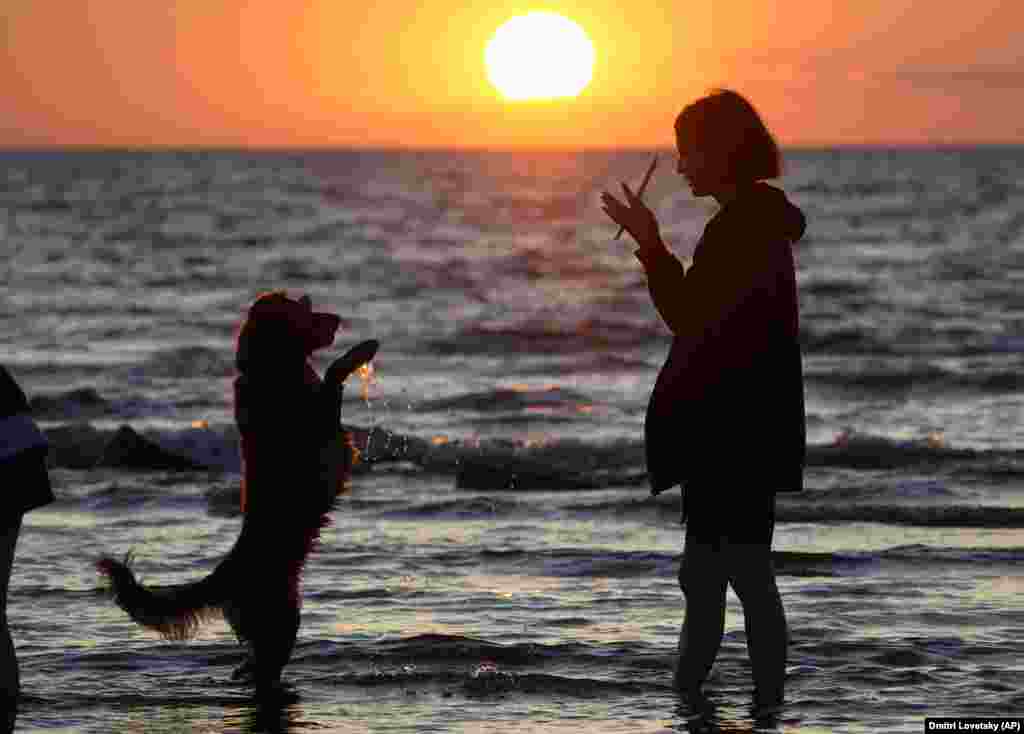 A woman plays with her dog at a beach on the Finnish Gulf as the sun sets in St. Petersburg, Russia.