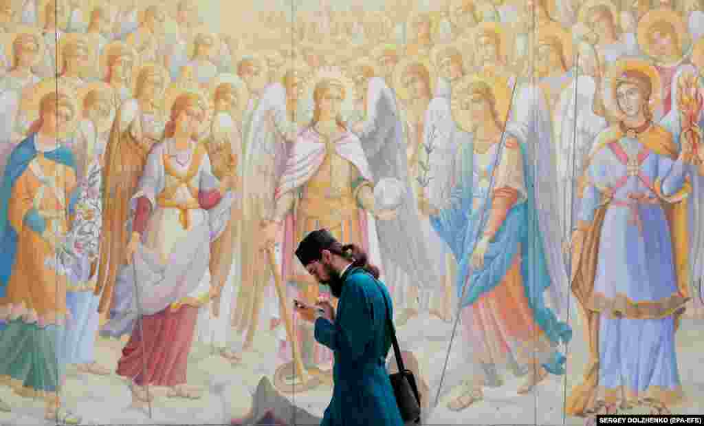 &nbsp;A priest looks at his mobile phone while walking past frescos on a wall of St. Michael&#39;s Cathedral in Kyiv.