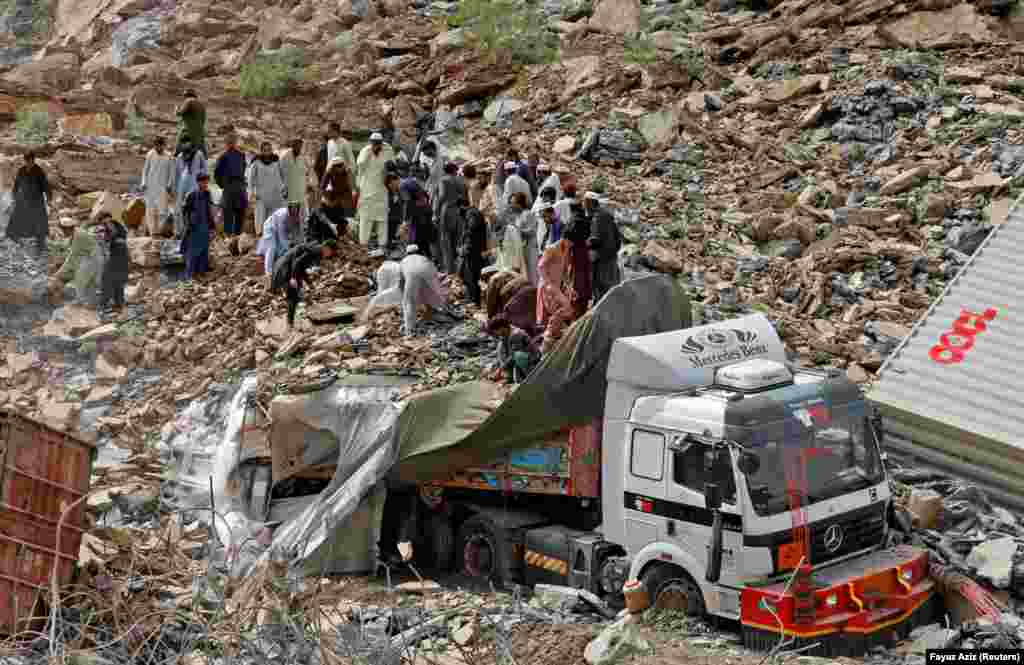 Rescue workers and people search for survivors next to a damaged supply vehicle.