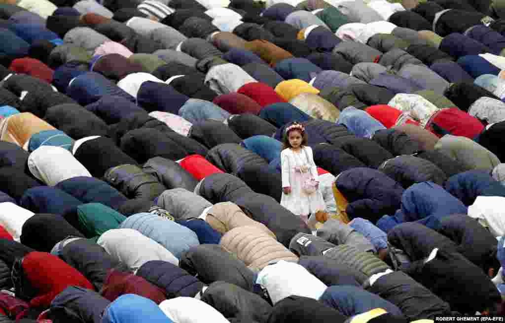 An aerial view shows Muslim worshippers saying morning prayers on the first day of Eid al-Fir at the Dinamo Sports Hall in Bucharest as a little girl,&nbsp;Hafsa Ahmend, looks on.