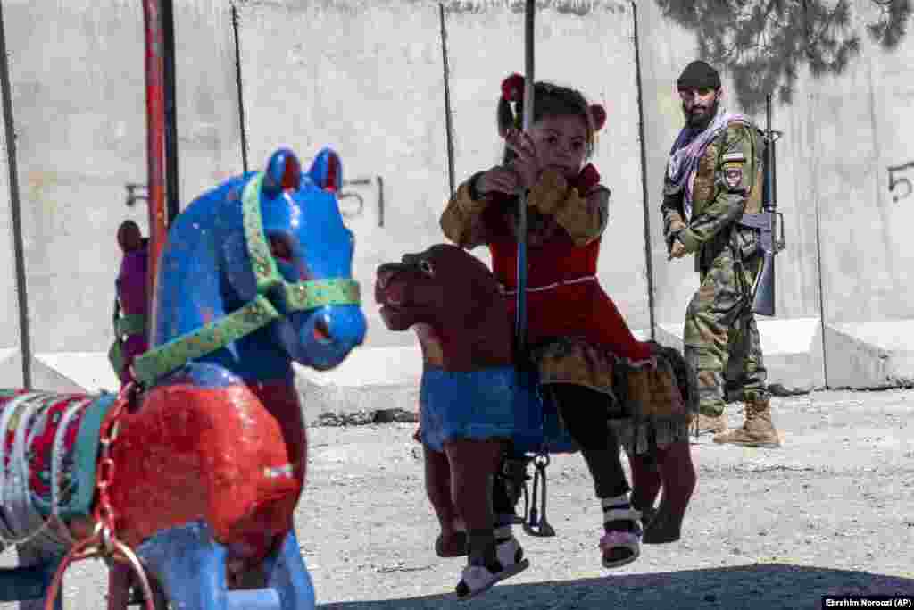 A Taliban fighter stands guard on Nadir Khan hill while a girl rides a merry-go-round during the first day of Eid al-Fitr in Kabul.