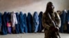 A Taliban fighter stands guard as women wait to receive food rations distributed by a humanitarian aid group in Kabul last month.