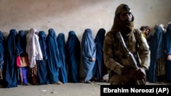 A Taliban fighter stands guard as women wait to receive food rations distributed by a humanitarian aid group in Kabul on May 23.