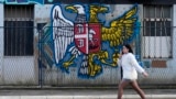 A girl walks by a mural on a wall that shows the Serbian (left) and Russian coats of arms in Belgrade.